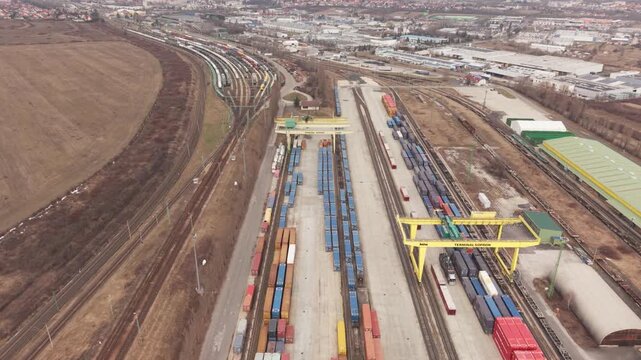 High angle drone view of a large intermodal freight terminal with rows of cargo containers and parallel railway tracks.