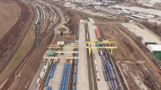 Aerial drone view of a large intermodal freight terminal with cargo containers and railway tracks. Yellow gantry cranes operate above long freight trains.