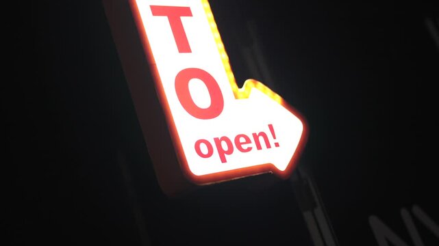 Illuminated open photobooth arrow sign glowing with warm lights during party event reveal in dark indoor venue &mdash; cinematic close up shallow depth of field shot.
