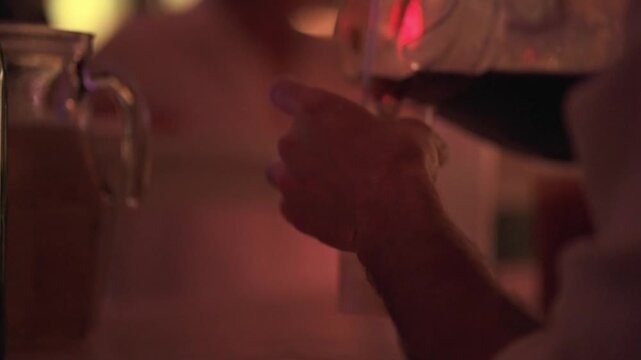 Hand pouring cold draft beer or dark beverage, creating a foamy head in a glass held at a lively evening bar, symbolizing celebration, refreshment, and social interaction