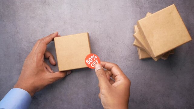 Person placing fifty percent off discount sticker on brown cardboard gift box for seasonal holiday sale promotion