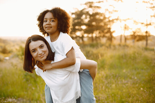 Caucasian mother holding her mixed race daughter on her back