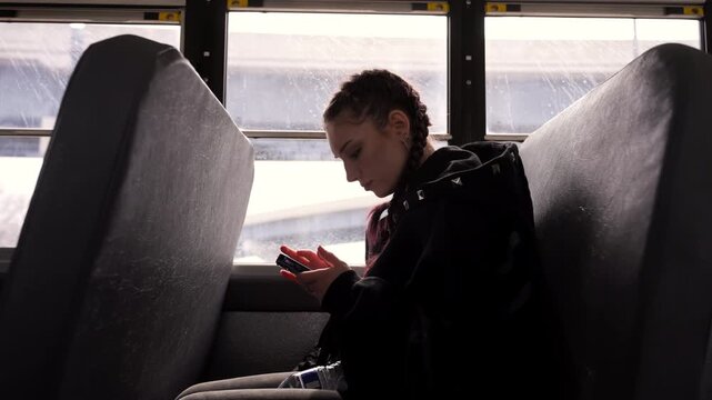 Student sitting in school bus seat using smartphone while traveling to or from school.