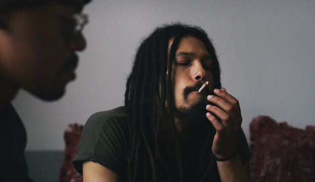 Weed, relax and friends with joint in home for smoking, bad habit and drugs at hangout on weekend. House, sofa and men with cannabis or marijuana for addiction, stress relief and unhealthy influence