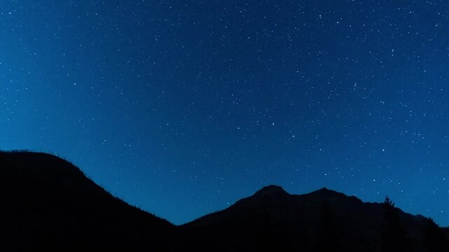 Stars appearing and moving over a dark mountain silhouette as twilight fades to night, Beartooth Mountains, Montana, time lapse