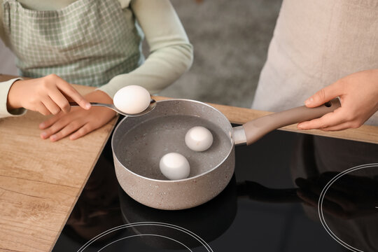 Little girl with her mother boiling eggs in kitchen, closeup