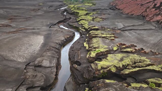 Volcanic ash landscape revealing a winding river creating a canyon through the dark terrain and patches of green vegetation, showing the raw power of nature and geological change on Tanna Island