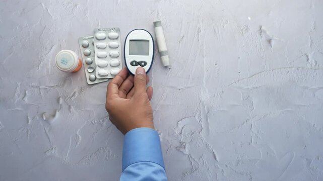 Person picking up glucose meter from table with medical supplies
