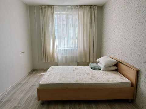 Bedroom with wooden bed and light curtains. Small empty room