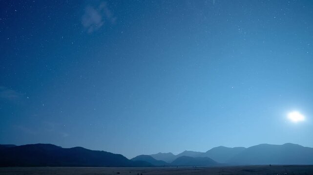 Moon rising over a mountain range into a starry sky as wispy clouds form and drift, Montana, time lapse