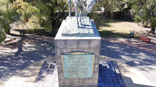Aerial camera descends toward the equestrian bronze statue of General Manuel Bulnes in Punta Arenas, Chile, featuring the large stone pedestal and the city's lush greenery
