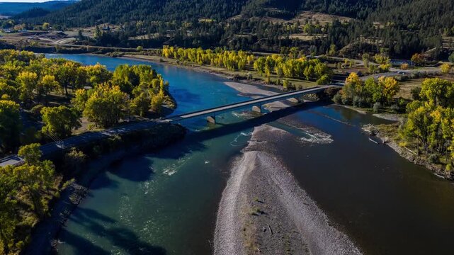 Aerial hyperlapse over the Yellowstone River and a bridge, then over pine covered hills toward the snowy Beartooth Mountains, Montana