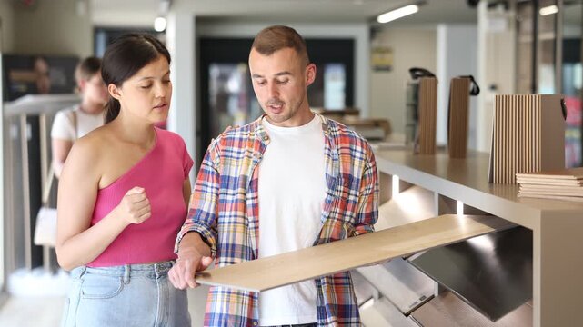 Girl and a friend choose laminate flooring in a hardware store. High quality 4k footage