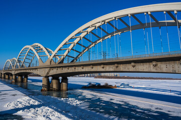 Obraz premium A wide-angle view of the white arched Binzhou Railway Bridge spanning the frozen, snow-covered Songhua River.