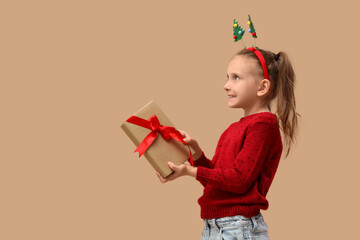 Naklejka premium Cute little girl with gift book on beige background. Christmas celebration