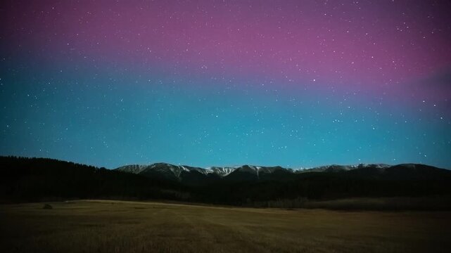 Pink northern lights glowing over the snowy Beartooth Mountains as moonlight brightens the sky, Montana, time lapse