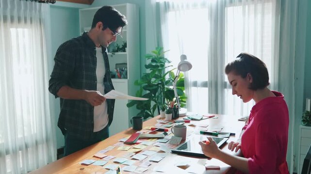 Top view of smart designer holding color palette while project manager looking at design and choosing color for program. Professional businesswoman taking a note while design creative logo. Symposium.
