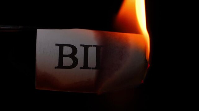 Sheet of paper with word BILL burning close-up on black background