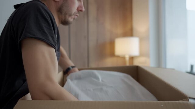 Person removes appliance covered in protective fabric from open cardboard box. Concept of appliance installation preparation and product unboxing process.