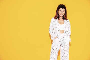 Obraz premium Young beautiful smiling female in trendy summer costume clothes. Carefree woman posing near yellow wall in studio. Positive model having fun indoors. Cheerful and happy