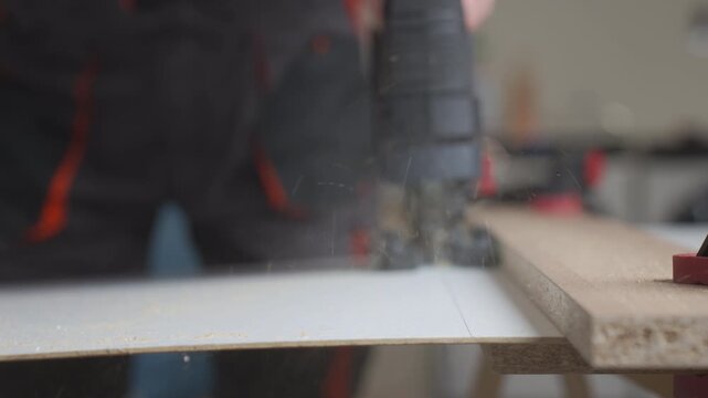 Close up of worker using electric jigsaw to cutting laminated board sheet in workshop