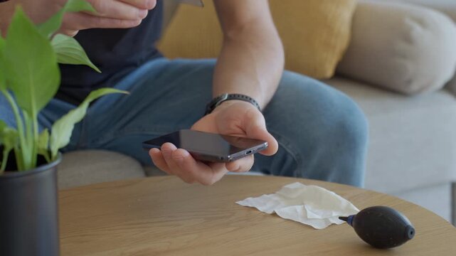 Man removing cracked protective glass screen protector from smartphone on wooden table. Concept of device repair screen protector replacement and mobile maintenance