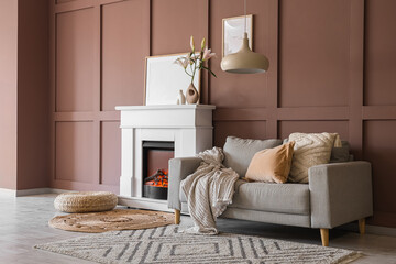 Naklejka premium Interior of cozy living room with grey sofa, wicker pouf and stylish fireplace