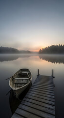 Fototapeta premium Rowboat docked at pier on misty lake at sunrise serene nature landscape