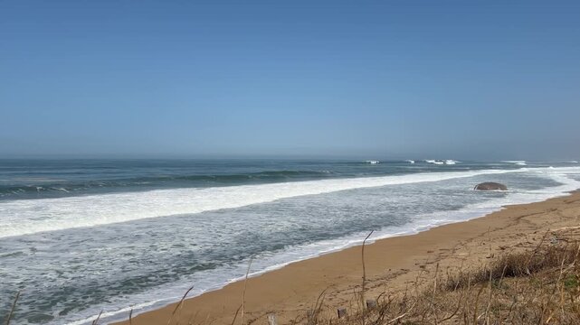 4K static shot of historic World War II bunkers covered in colorful graffiti on a sandy beach. Atlantic Ocean waves crash against the concrete ruins on a sunny day in Labenne, Landes, France. Cinemati