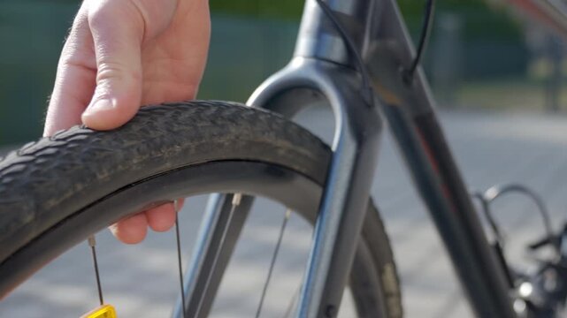Hand squeezes bicycle tire to check pressure after puncture on bike on paved street. Flat bicycle tire during ride. Concept of cycling service and bike maintenance