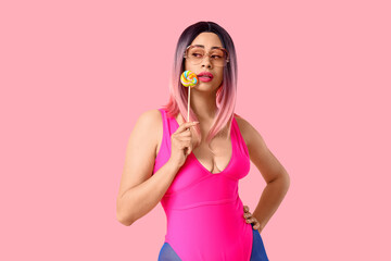 Beautiful young African-American woman in stylish wig and sunglasses with sweet lollipop on pink...