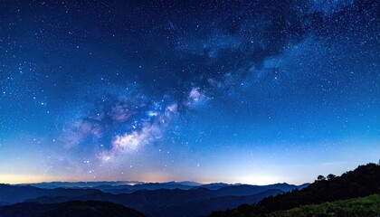 Vast panoramic nightscape showcasing the Milky Way arching across a vibrant indigo sky above distant mountain silhouettes