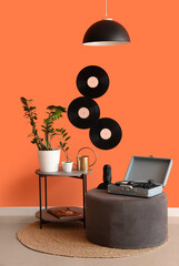 Table, pouf, record player and houseplants near orange wall in room
