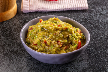 Freshly made chunky guacamole in a purple bowl on a dark stone background.
