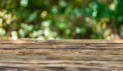 Fototapeta premium Green background with wooden table. Wooden table in the foreground with a lush, green park scene in the background. Beautiful natural summer background with empty wooden table in nature outdoor.