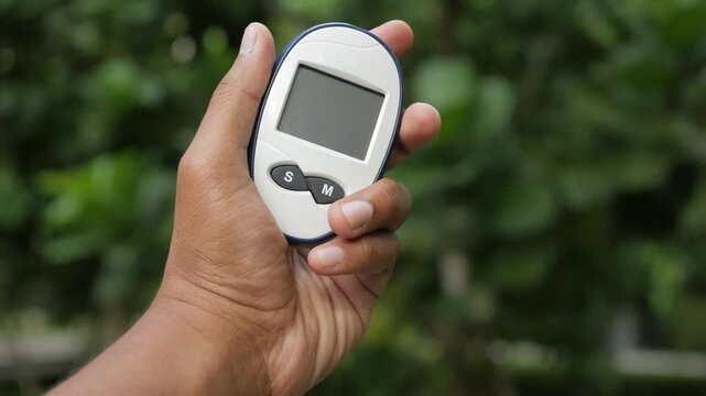 Close up slow motion footage of male hand holding glucometer on green background, device to measure blood sugar level