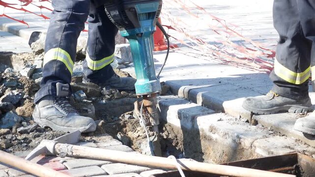 Construction workers use jackhammer to break pavement for road repair