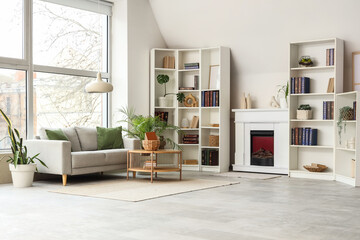 Naklejka premium Shelves with books, sofa and fireplace in interior of modern living room