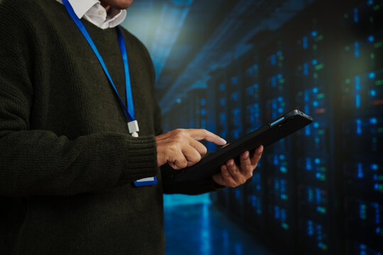 Close-up of a person with lanyard using a tablet in a data center corridor with glowing server lights, concept of it admin, cybersecurity, cloud computing, network monitoring