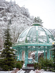 Fototapeta premium Winter scene of a glass gazebo in a snowy landscape with trees and a mountain background