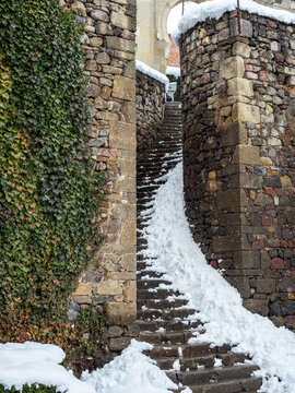 Ancient stone staircase leading to an archway in Rabati Castle, Georgia, during winter, featuring ivy-covered walls and fresh white snow on the steps