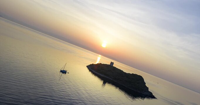Aerial sunset hyperlapse scene of a small island with a historic tower and anchored sailboat off Pula, Croatia.