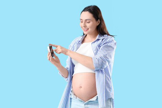 Young pregnant woman using glucometer on blue background. Gestational diabetes concept