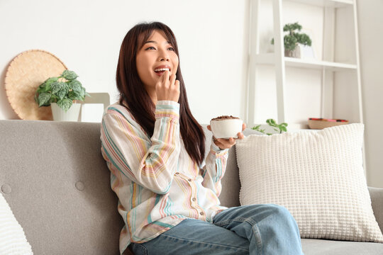 Young Asian woman eating fried insects on sofa at home