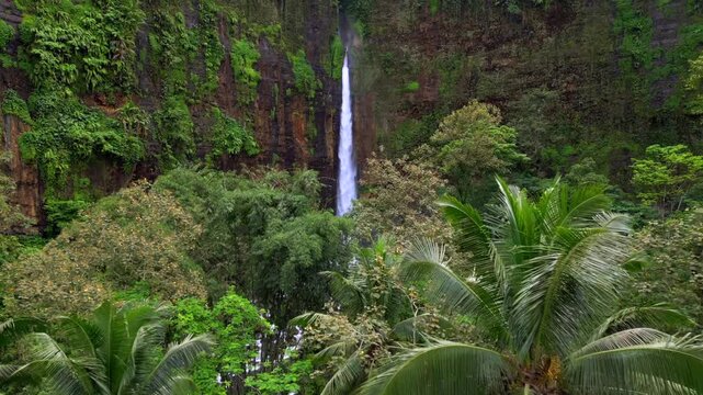 Aerial drone view of Kapas Biru waterfall surrounded by lush tropical jungle in East Java, Indonesia. Scenic rainforest landscape with tall cascade and mist in Southeast Asia.