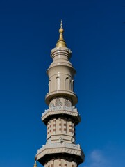 A tall mosque minaret with a golden tip standing against a clear blue sky. The Islamic architectural tower symbolizes spirituality, worship, and religious culture.