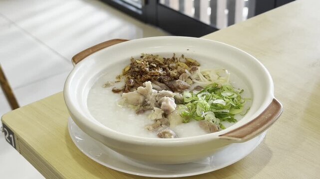 Hot Chinese-style chicken congee served in traditional claypot, topped with fresh scallions and visible steam rising. Warm comfort food concept with authentic Asian cuisine,