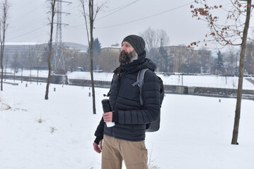 Man in black puffer jacket with backpack and thermos in a snowy park © salajean