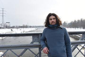 Man with long curly hair standing on a metal bridge wearing a blue fleece pullover in winter © salajean