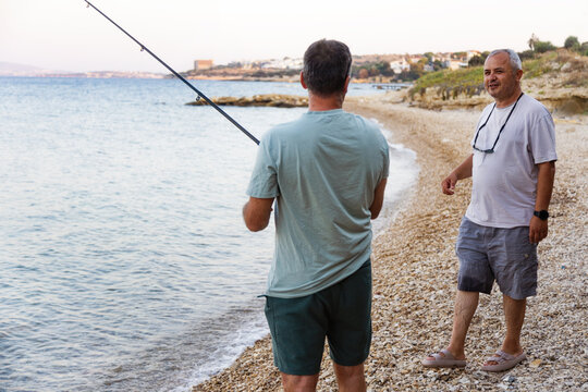 Two men fishing and talking on rocky beach